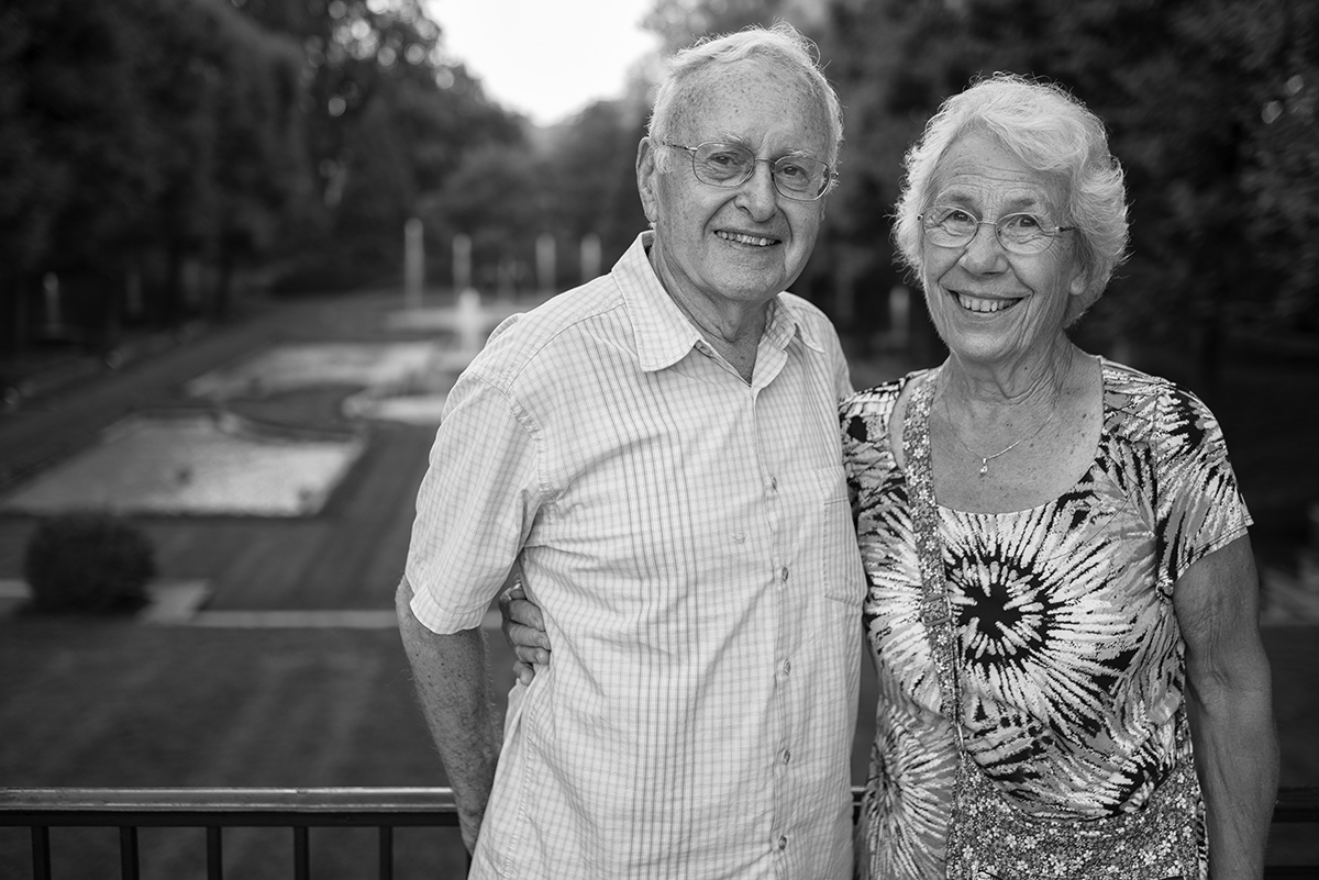 Um casal de idosos sorridente posa junto em preto e branco - um exemplo de como fotografar retratos de família que honram o amor duradouro e o legado. ©Ken Hubbard