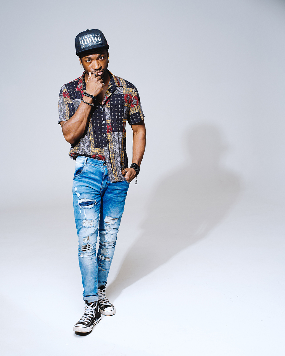 Portrait en studio d'un homme en jean déchiré, chemise à motifs et casquette, éclairé par une lumière claire et intense. L'image met en évidence les techniques d'éclairage de portrait pour le caractère, en utilisant des ombres contrôlées et la posture pour mettre en valeur le style et la personnalité.