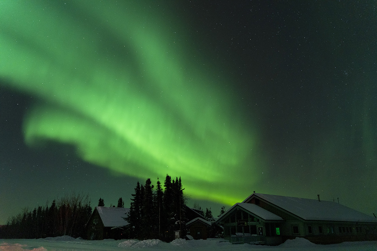 A mesmerizing image of the Northern Lights, which create vibrant green colors dancing in the night sky above snow covered cabins. 