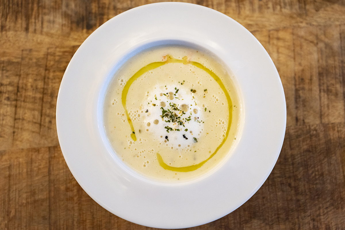 Creamy soup garnished with herbs and olive oil, captured with a Tamron prime lens for Sony E-mount, highlighting food photography detail.
