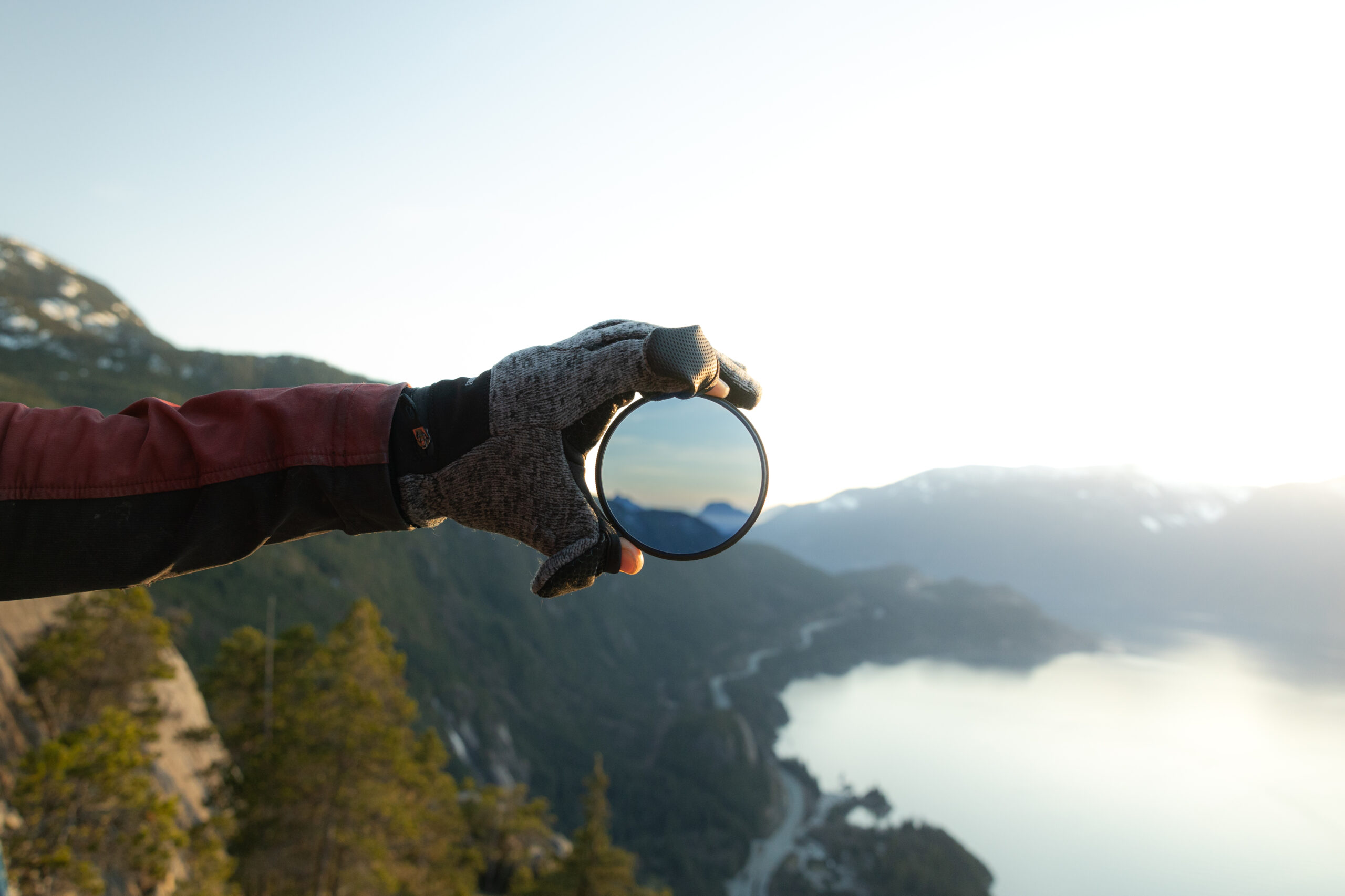 Photographer holding a ProMaster circular polarizer (CPL) filter, demonstrating how to use a circular polarizer to enhance landscape photography by reducing glare, improving contrast, and enriching colors.