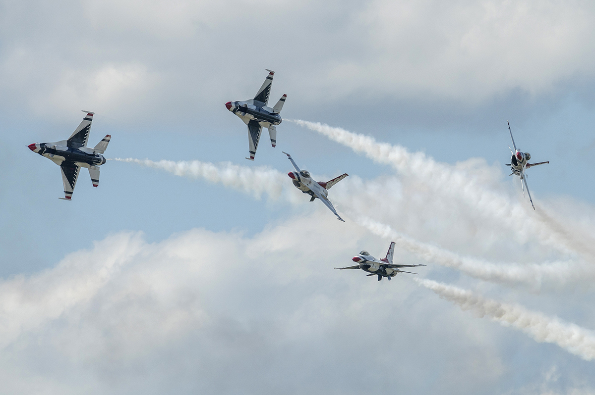 USAF Thunderbirds perform a dramatic aerial maneuver with smoke trails cutting across the sky&mdash;an action-filled moment captured using Tamron lenses for airshow photography.