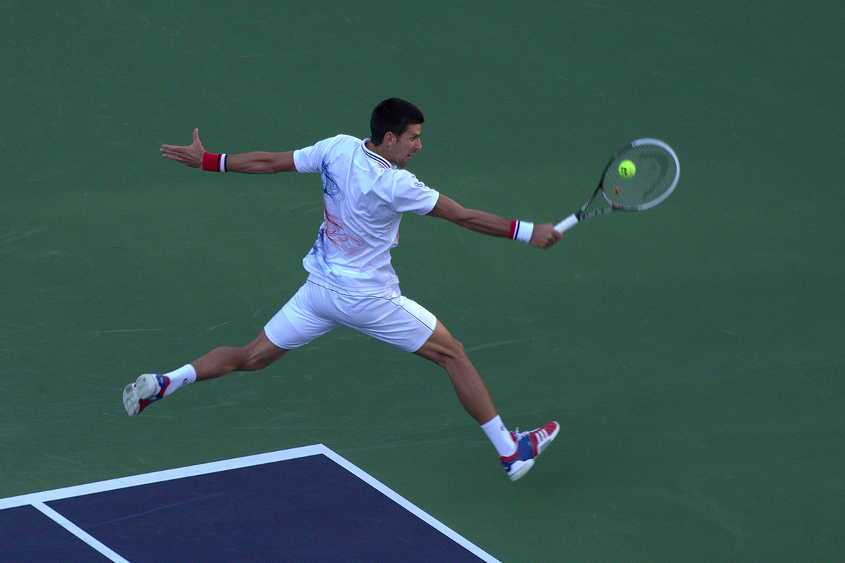 Un jugador de tenis salta en el aire para conseguir un potente disparo en la pista: un ejemplo ideal de captura del movimiento utilizando consejos para fotografía deportiva.