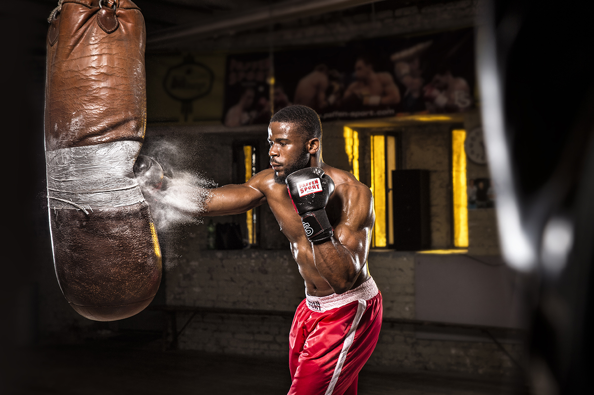 A muscular boxer in red shorts punches a heavy bag, with powder bursting from impact under dramatic lighting&mdash;an example of how to get a cinematic look through dynamic action, contrast, and atmosphere.