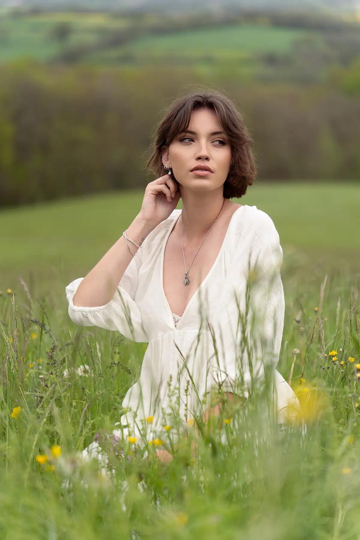 Femme en robe blanche assise dans une prairie de fleurs sauvages, doucement éclairée par un éclairage naturel de photographie d'été dans un champ ouvert.