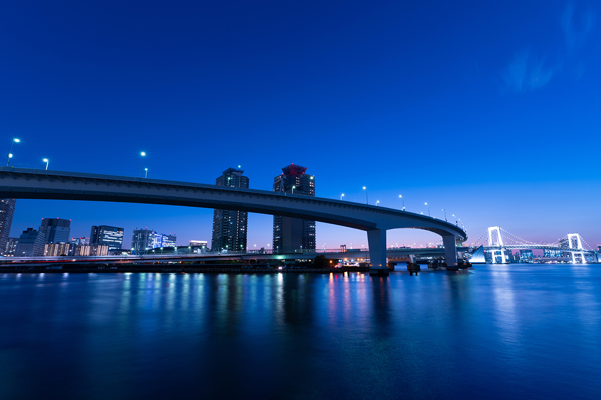 A cityscape featuring a long curved bridge illuminated by street lights at dusk, enhanced through long exposure photo editing.