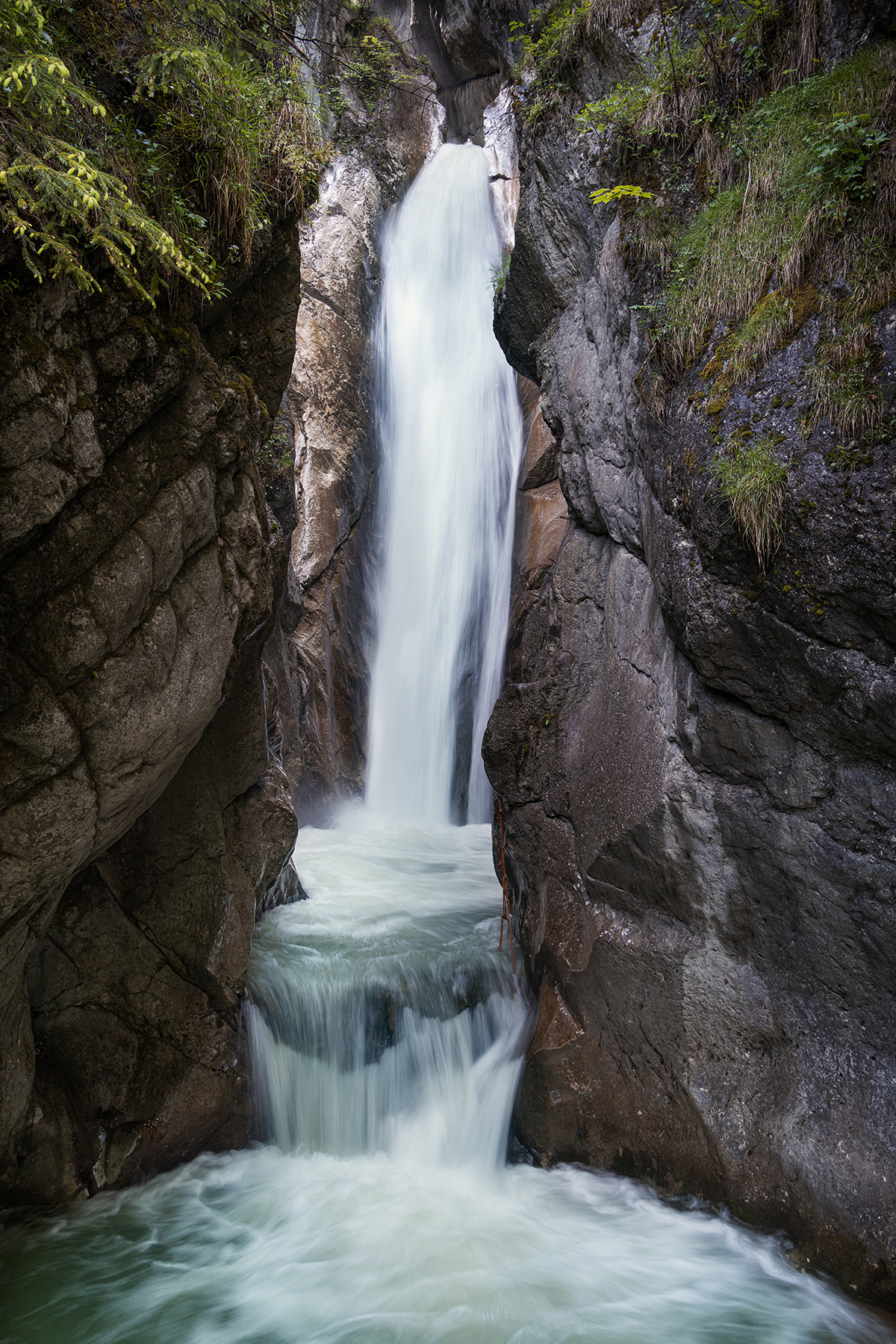 A cascading waterfall between two cliffs with greens.