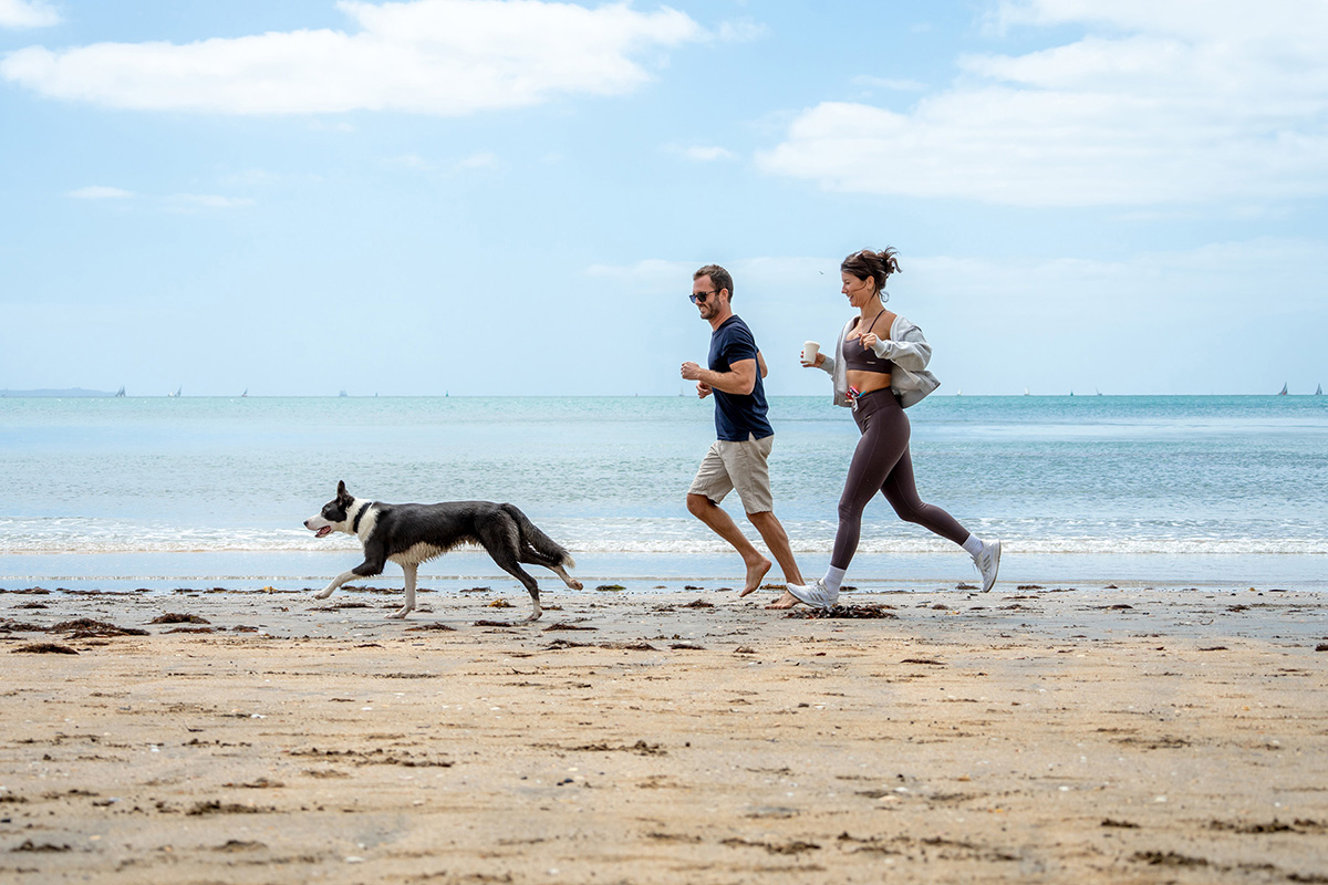 Casal correndo com o cachorro na praia