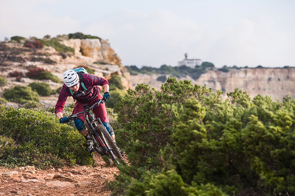 Mountain biker carving through a rugged trail with scenic cliffs in the background&mdash;capturing dynamic action shots with fast lenses.