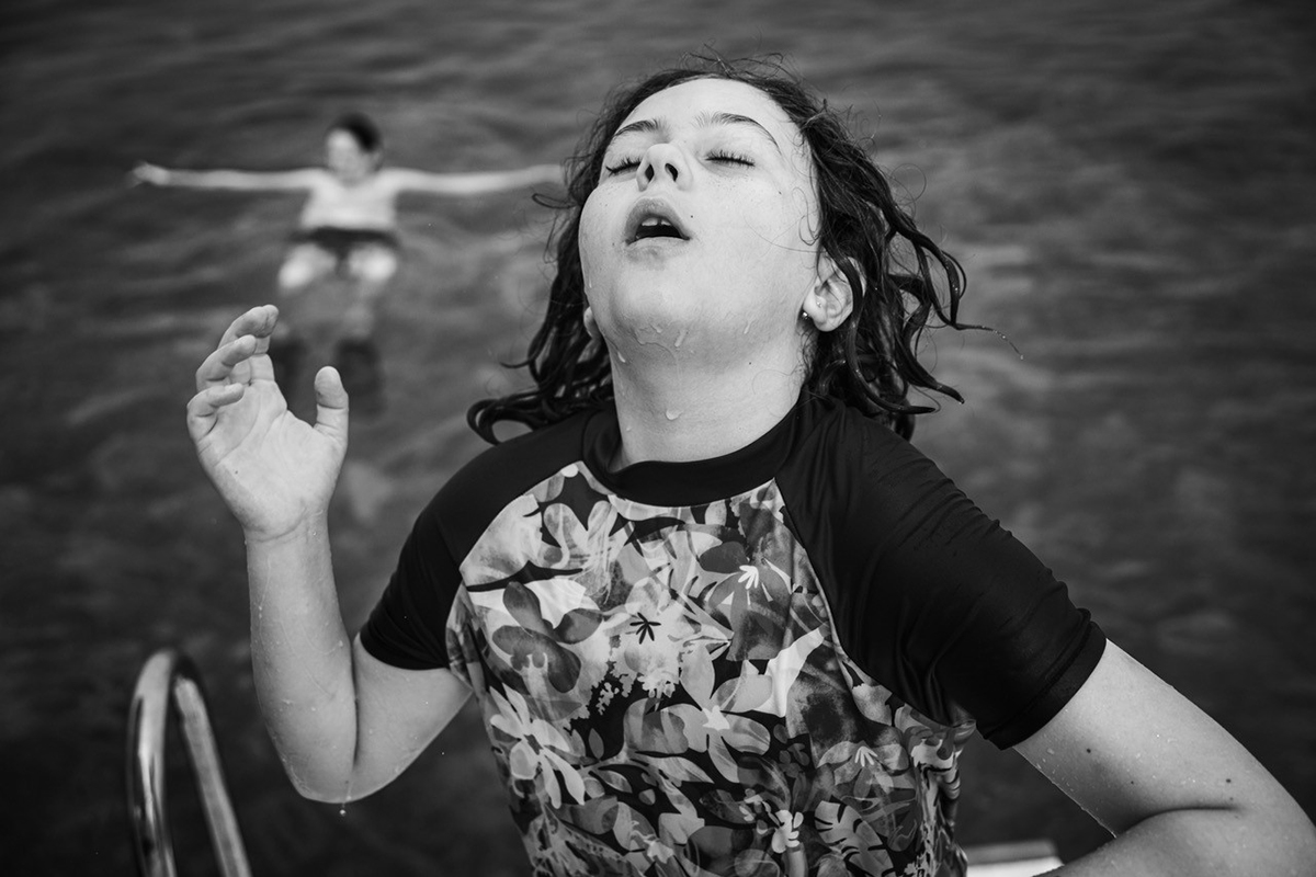 Una foto en blanco y negro de una niña saliendo del agua con los ojos cerrados y gotas de agua en la cara, que ilustra cómo contar una historia con la fotografía a través de la emoción y el momento. ©Andre Costantini
