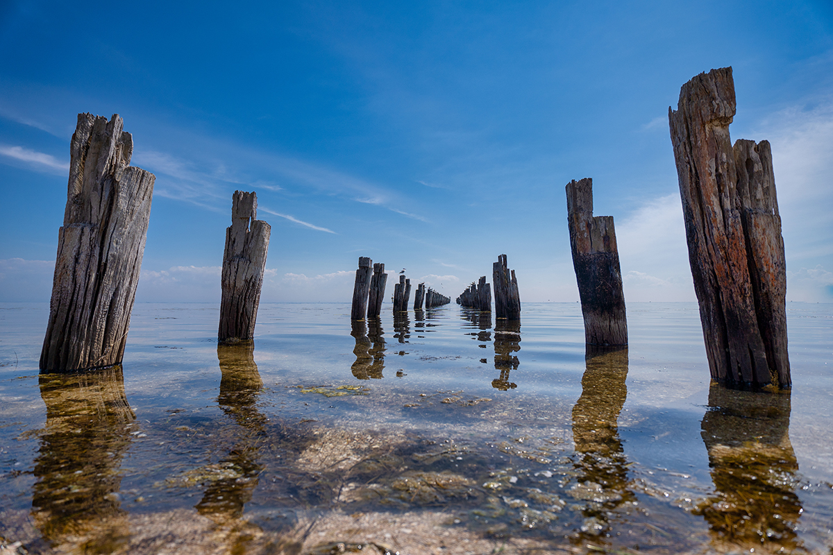 Striking view of wooden pilings reflected in calm water, captured with a circular polarizer filter to deepen sky blues, enhance clarity, and reduce surface reflections.
