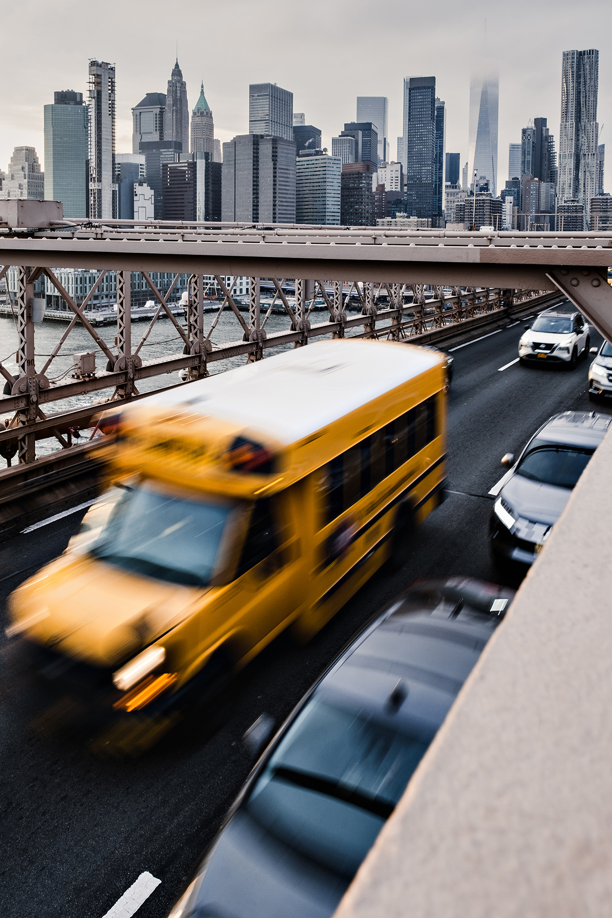 Una toma de un puente urbano muy transitado en la que destaca un autobús escolar amarillo, realizada con fotografía de larga exposición para crear sensación de movimiento.