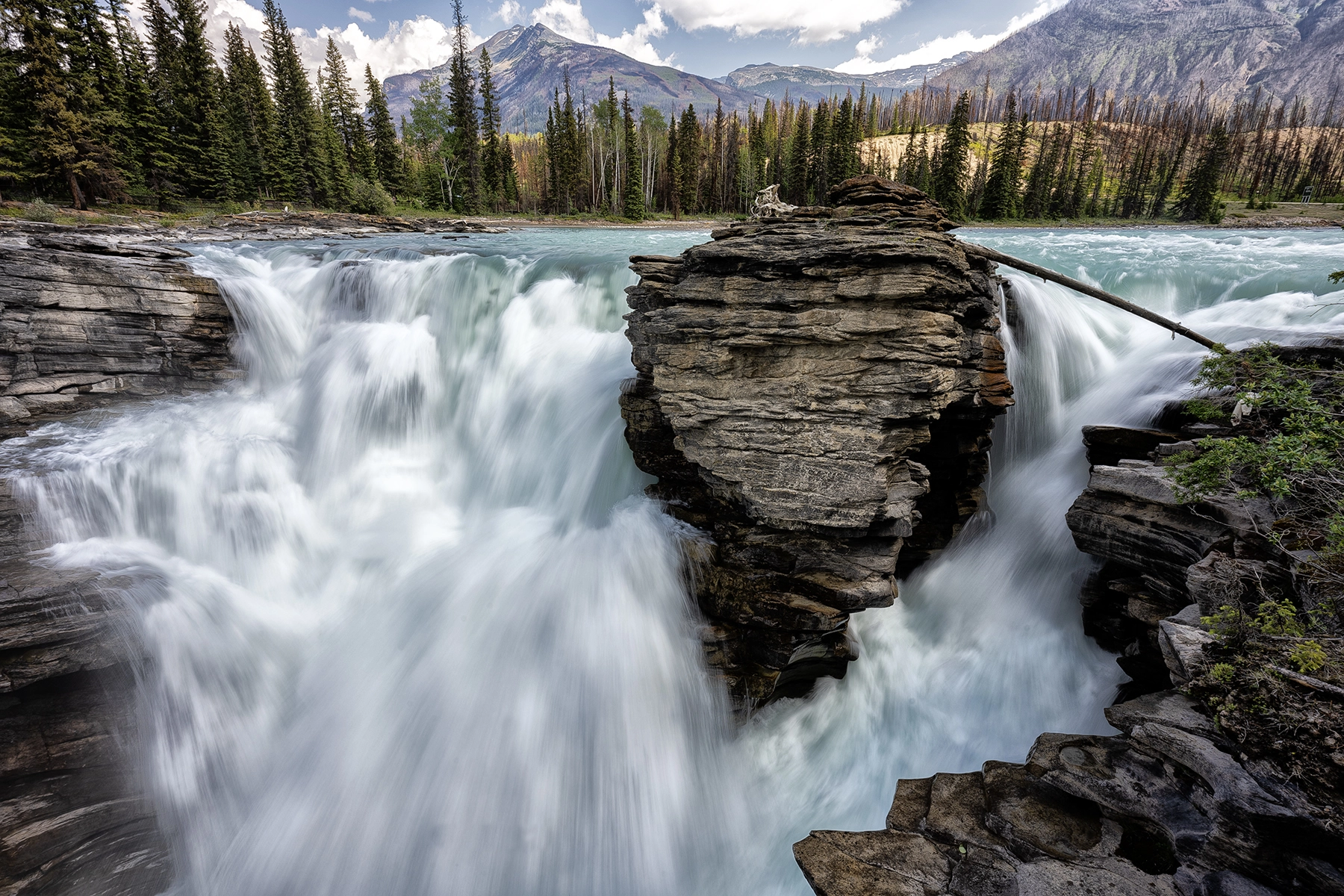A rushing waterfall against below mountains achieved using long exposure photography.