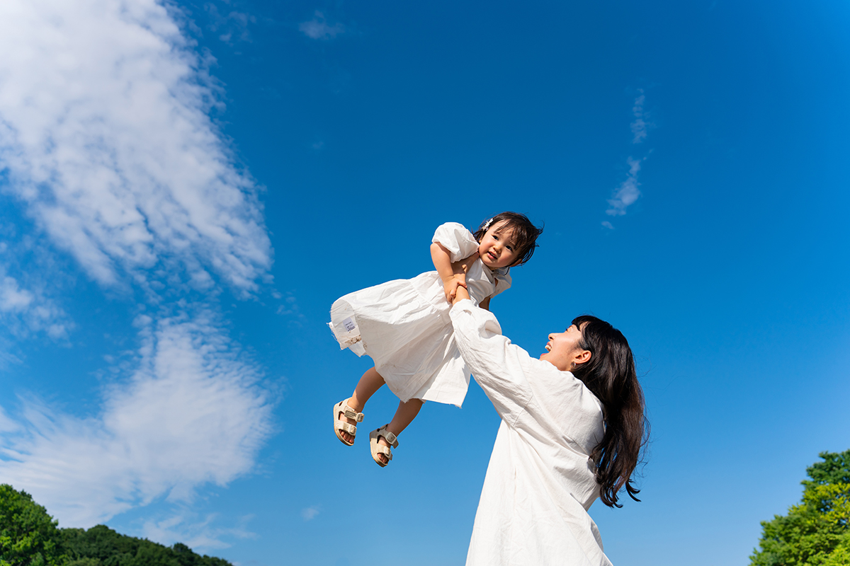 Alegre momento de una madre levantando a su hijo al aire libre, capturando emociones genuinas con consejos para retratos del Día de la Madre.