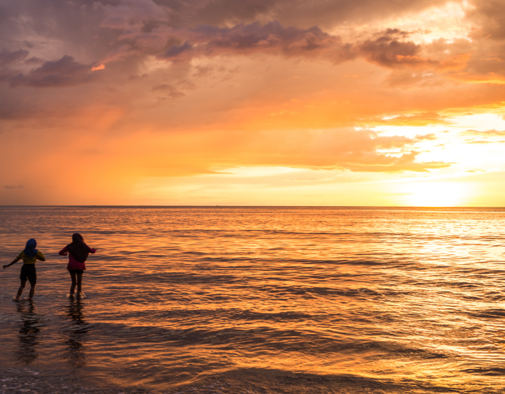 Duas pessoas na praia durante o pôr do sol com um céu laranja e amarelo