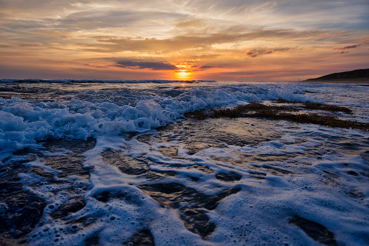 Sunrise over ocean waves crashing on a beach with glowing clouds, captured using the best settings for sunset and sunrise photos.