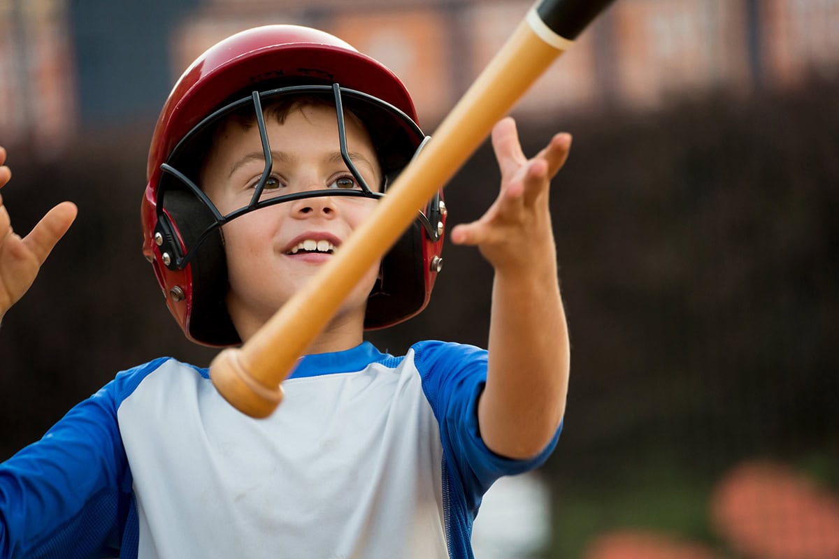 Jogador de beisebol da Liga Infantil sorrindo e jogando um taco no ar - capturado em um momento espontâneo enquanto fotografava a Liga Infantil de beisebol.