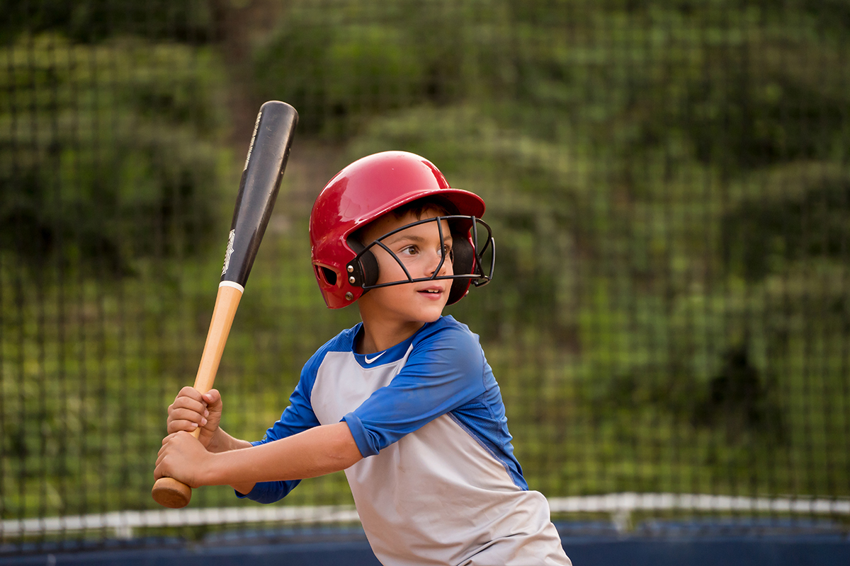 Jovem jogador de beisebol da Little League no bastão, usando um capacete vermelho, concentrado e pronto para bater - capturado enquanto fotografava a ação de beisebol da Little League.