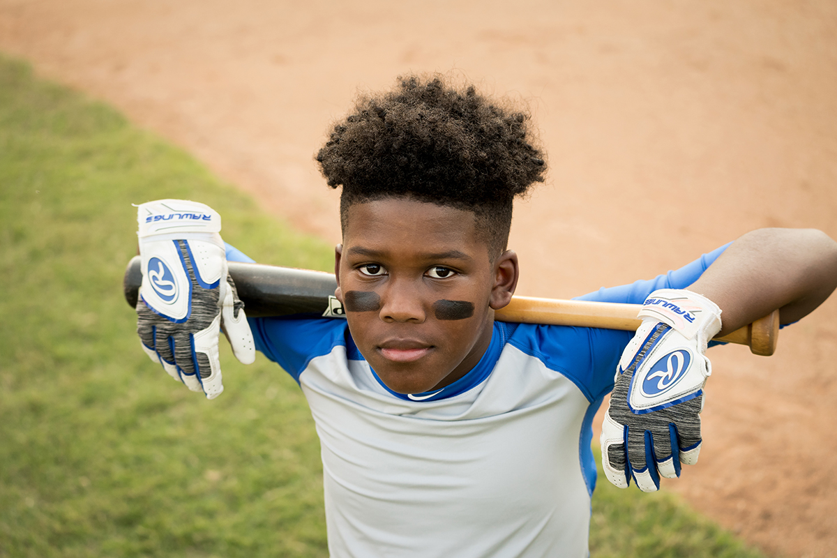 Jovem jogador de beisebol da Liga Infantil em pé, confiante, com um taco sobre os ombros, exemplo perfeito para fotografar o beisebol da Liga Infantil com emoção e impacto.