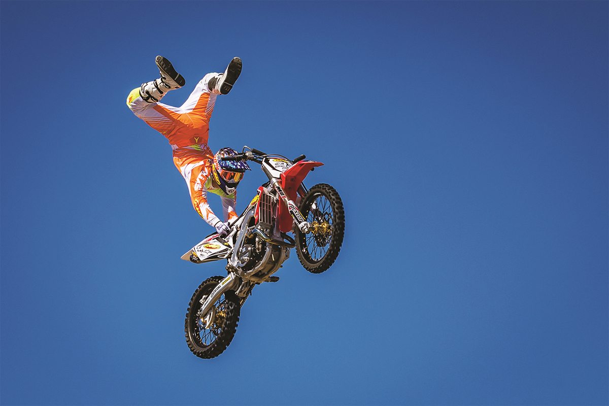 Un piloto de motocross en pleno vuelo durante una acrobacia contra un cielo azul despejado: un ejemplo lleno de acción para consejos de fotografía deportiva.