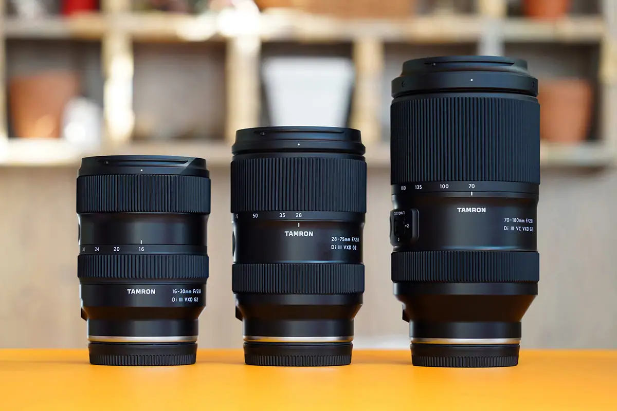 A group shot of Tamron's fast aperture G2 trinity lenses - 16-30mm, 28-75mm, and 70-180mm standing on a yellow table.