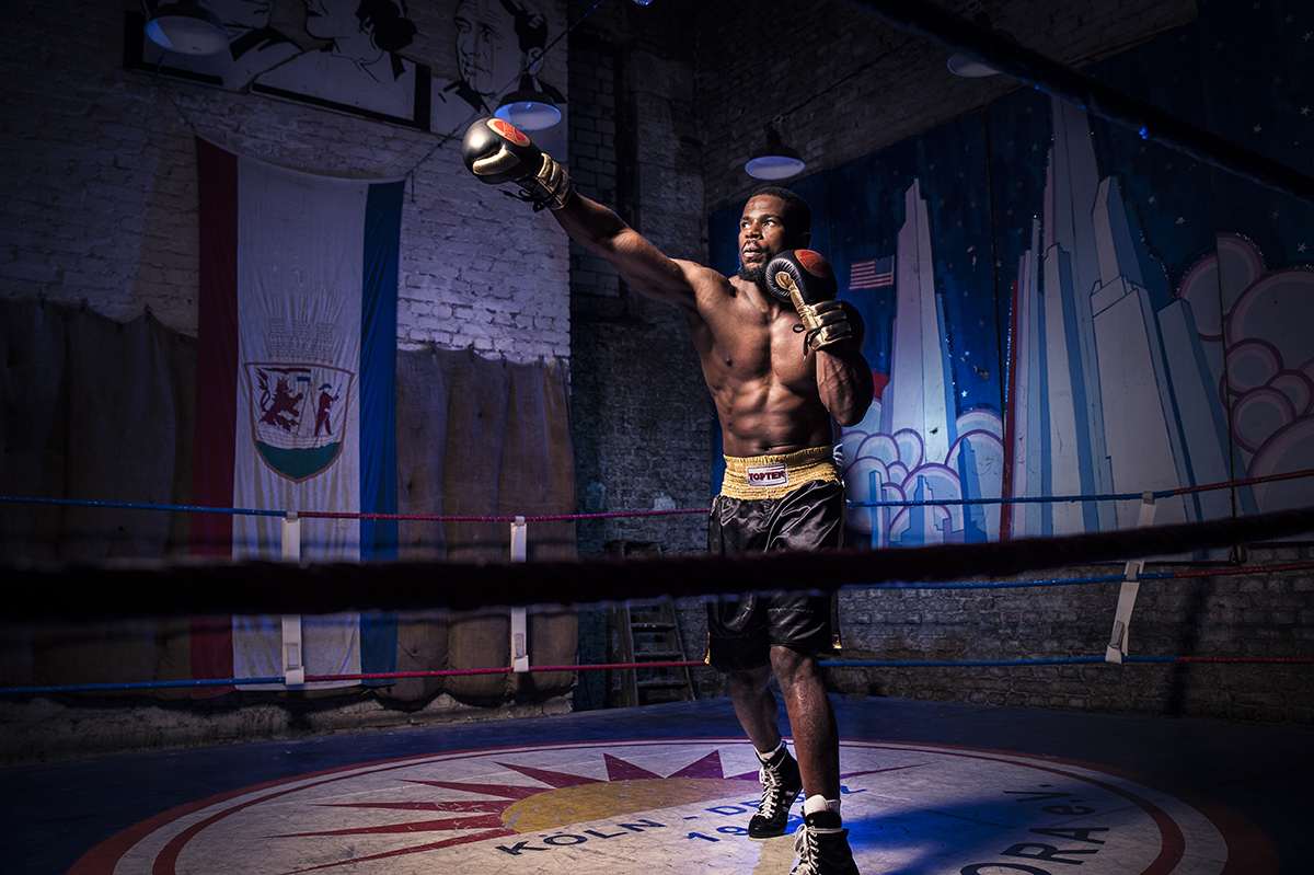 Un dramático retrato con poca luz de un boxeador en pleno golpe en un gimnasio poco iluminado, mostrando músculos definidos, sombras controladas y una fuerte iluminación direccional: un ejemplo de fotografía de retrato experta con poca luz en acción.