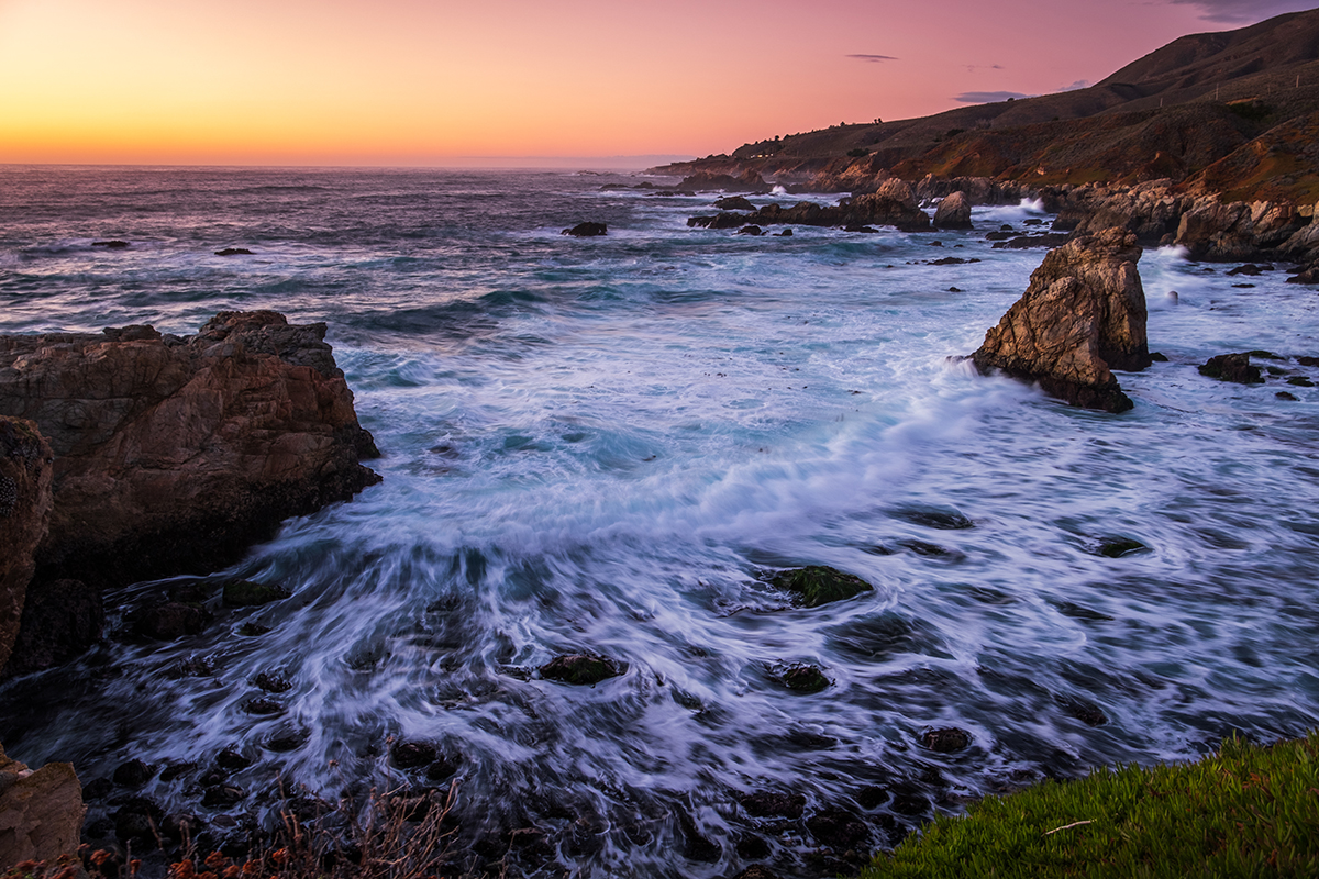 Vibrant waves crashing against rocky cliffs at sunset along the coast&mdash;ideal composition to showcase beach sunset photography tips in action.