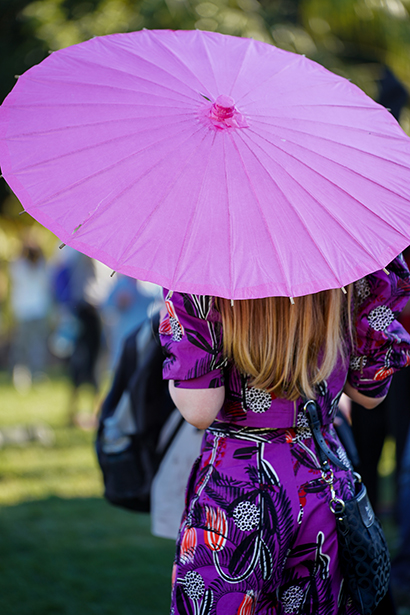 Uma mulher em um vestido estampado segurando uma sombrinha rosa brilhante - ilustrando como tirar fotos de rua capturando cores ousadas e estilo pessoal. ©Janet Vuong