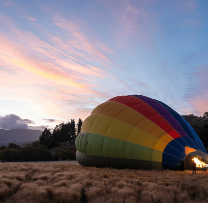 Photo de coucher de soleil d'une montgolfière colorée en train d'être gonflée dans un champ ouvert, avec un ciel pittoresque et des nuages doux en arrière-plan.