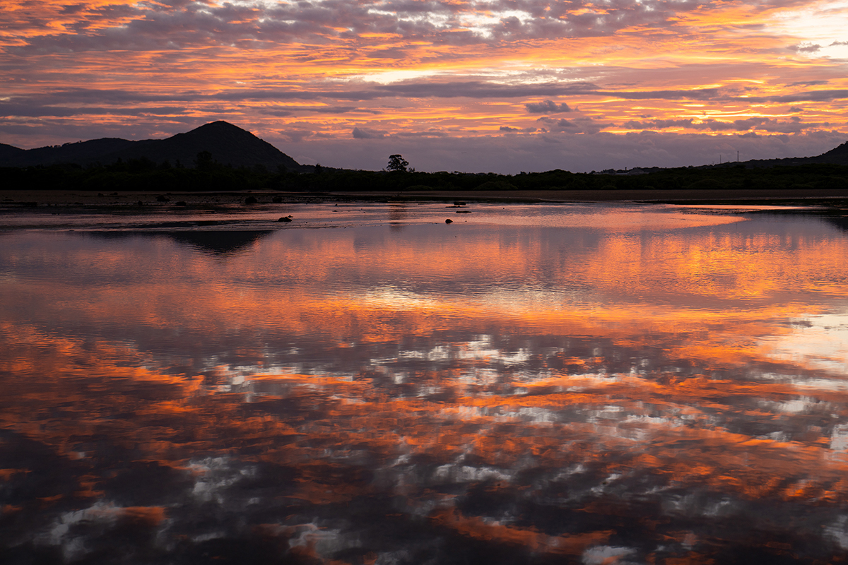 Impresionante paisaje al atardecer que muestra las vibrantes tonalidades anaranjadas y púrpuras de la hora dorada reflejadas en un tranquilo lago: un ejemplo de dominio de la iluminación exterior en la fotografía de naturaleza. ©Kiyotaka Kitajima