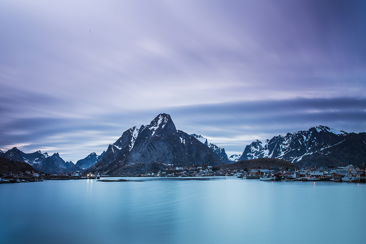 Des montagnes enneigées se reflétant dans un fjord gelé et immobile pendant l'heure bleue - une scène idéale pour tester les techniques d'entretien du matériel de photographie d'hiver dans des conditions extrêmes.