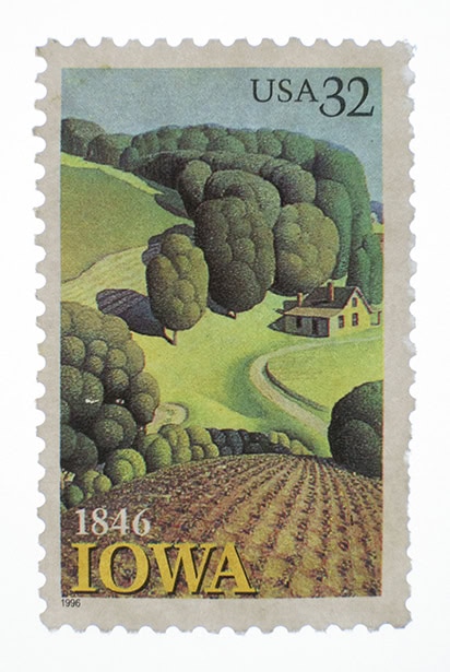 A 32-cent USA postage stamp commemorating Iowa&rsquo;s statehood in 1846, featuring a stylized rural landscape with fields, trees, and a farmhouse. &copy;Jillian Bell