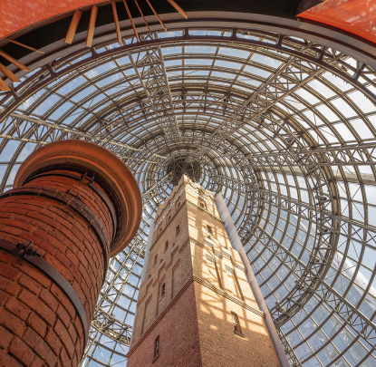 Brick tower enclosed within a massive glass and steel dome structure, viewed from a low-angle perspective.