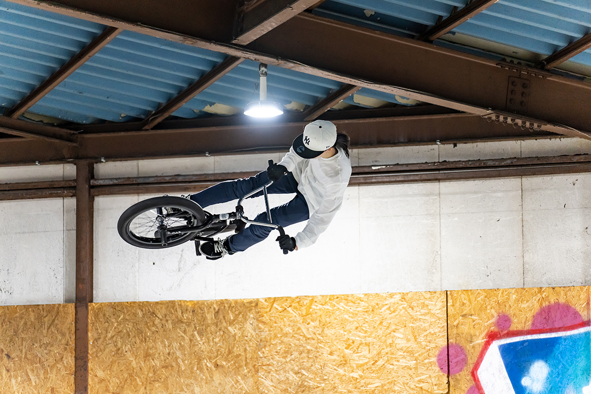 Un corredor de BMX ejecuta un truco aéreo bajo unas vigas industriales, capturado mientras fotografiaba deportes extremos con el TAMRON 35-150 mm F2-2,8.