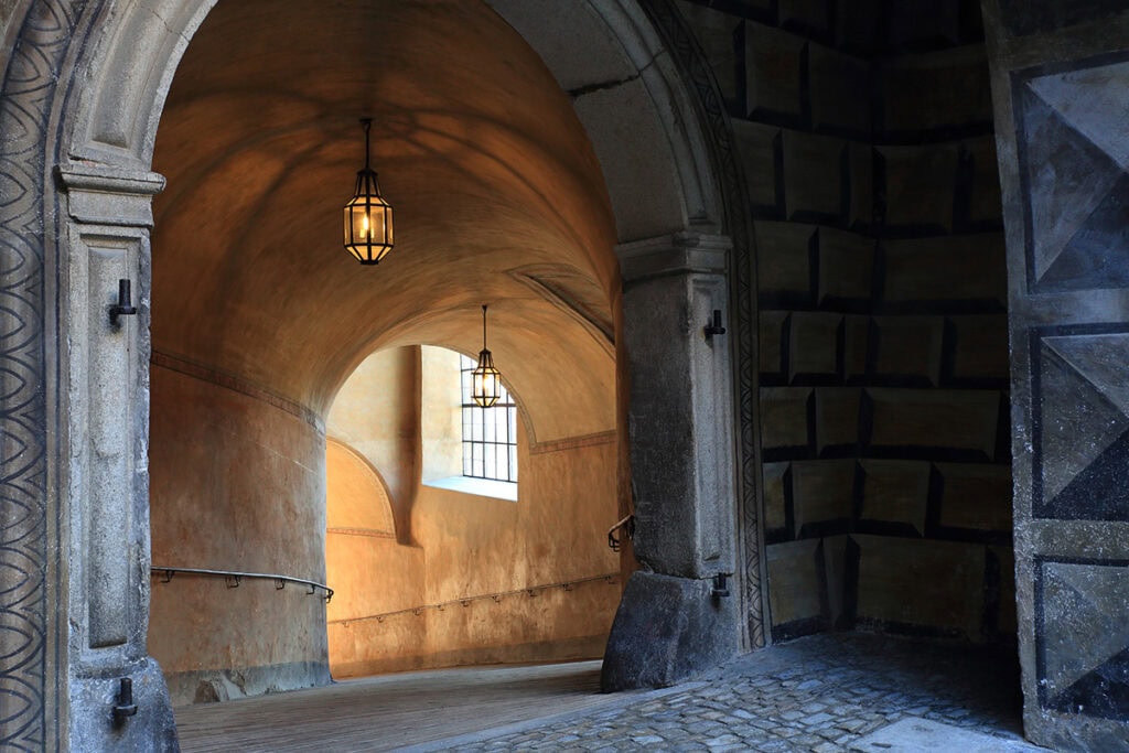 Couloir en pierre incurvé avec des plafonds voûtés et des lanternes, mettant en valeur la profondeur, la symétrie et les lignes directrices - parfait pour les conseils en photographie d'architecture.