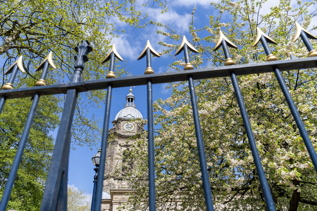 Tour d'horloge historique encadrée par une clôture en fer décorative et des arbres en fleurs, illustrant l'utilisation créative de la perspective dans les conseils de photographie d'architecture.