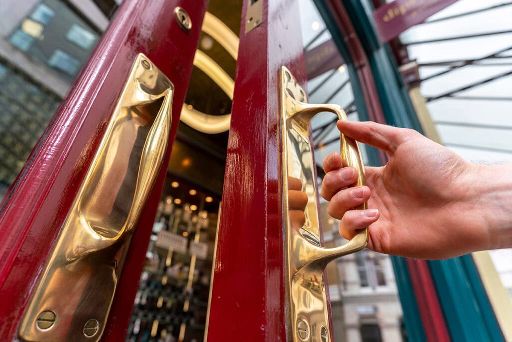 Gros plan d'une main ouvrant une porte rouge à poignée en laiton, capturant de fins détails architecturaux - idéal pour les conseils de photographie d'architecture sur les textures.
