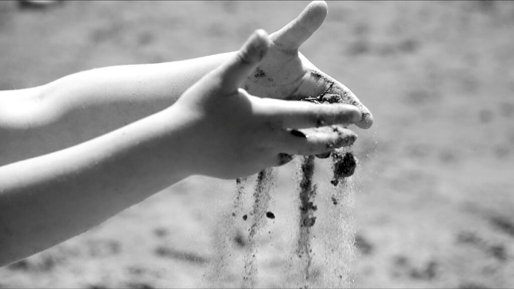 A black and white close-up picture of a child&rsquo;s hands playing with sand on a beach.