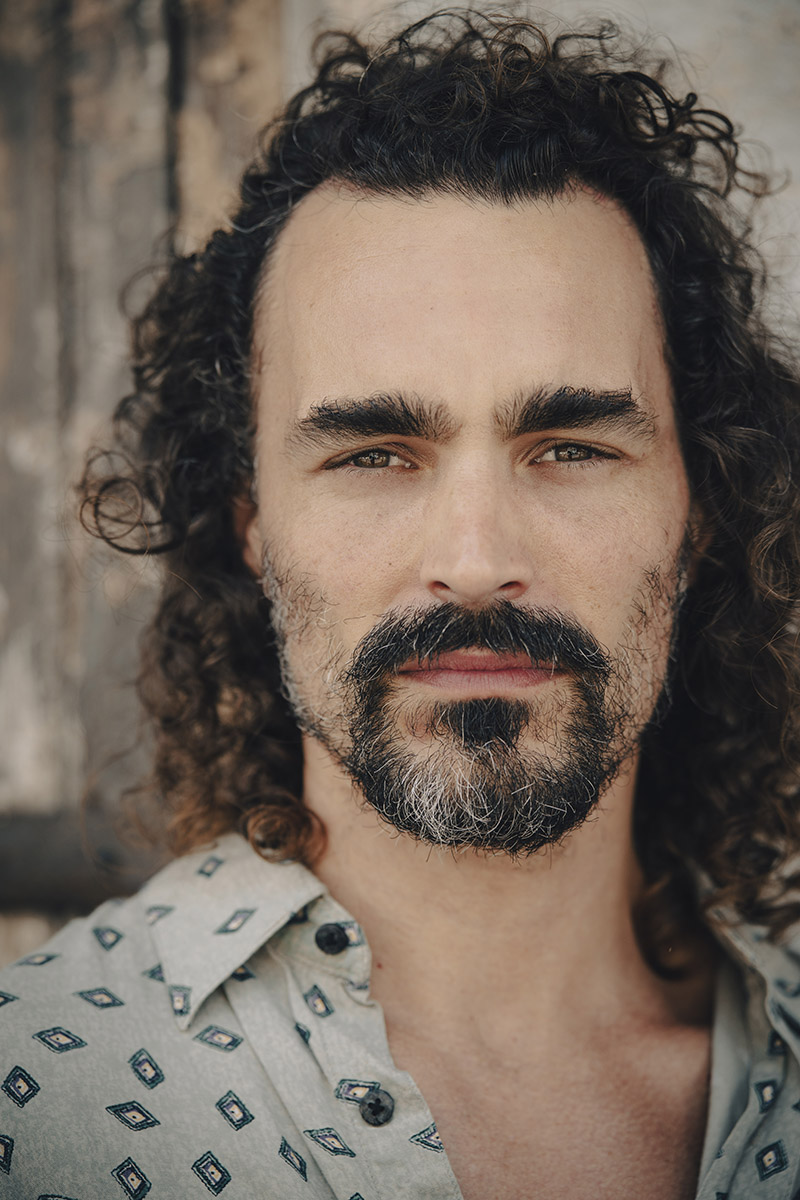 Retrato en primer plano de un hombre con pelo largo y rizado y barba.