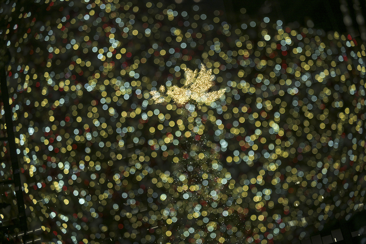 Uma decoração de anjo brilhante brilha intensamente em meio a um impressionante bokeh de luzes natalinas.