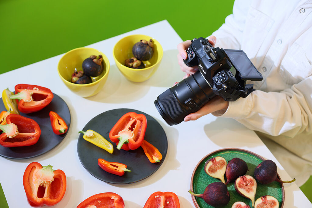 Photographe utilisant un objectif Tamron sur un appareil photo Nikon pour capturer des produits frais, appliquant des conseils de photographie macro pour des gros plans d'aliments éclatants.