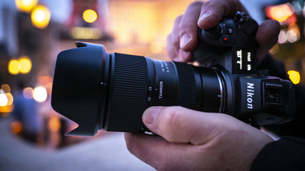 A photographer wearing an orange shirt adjusts a Nikon camera with one of the best Nikon Z lenses for wildlife mounted on a tripod.