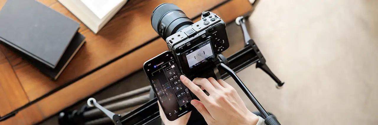 Fotógrafo utilizando la aplicación móvil TAMRON Lens Utility™ Ver. 5.0 para controlar el enfoque y los ajustes del objetivo durante una sesión fotográfica con un slider motorizado.