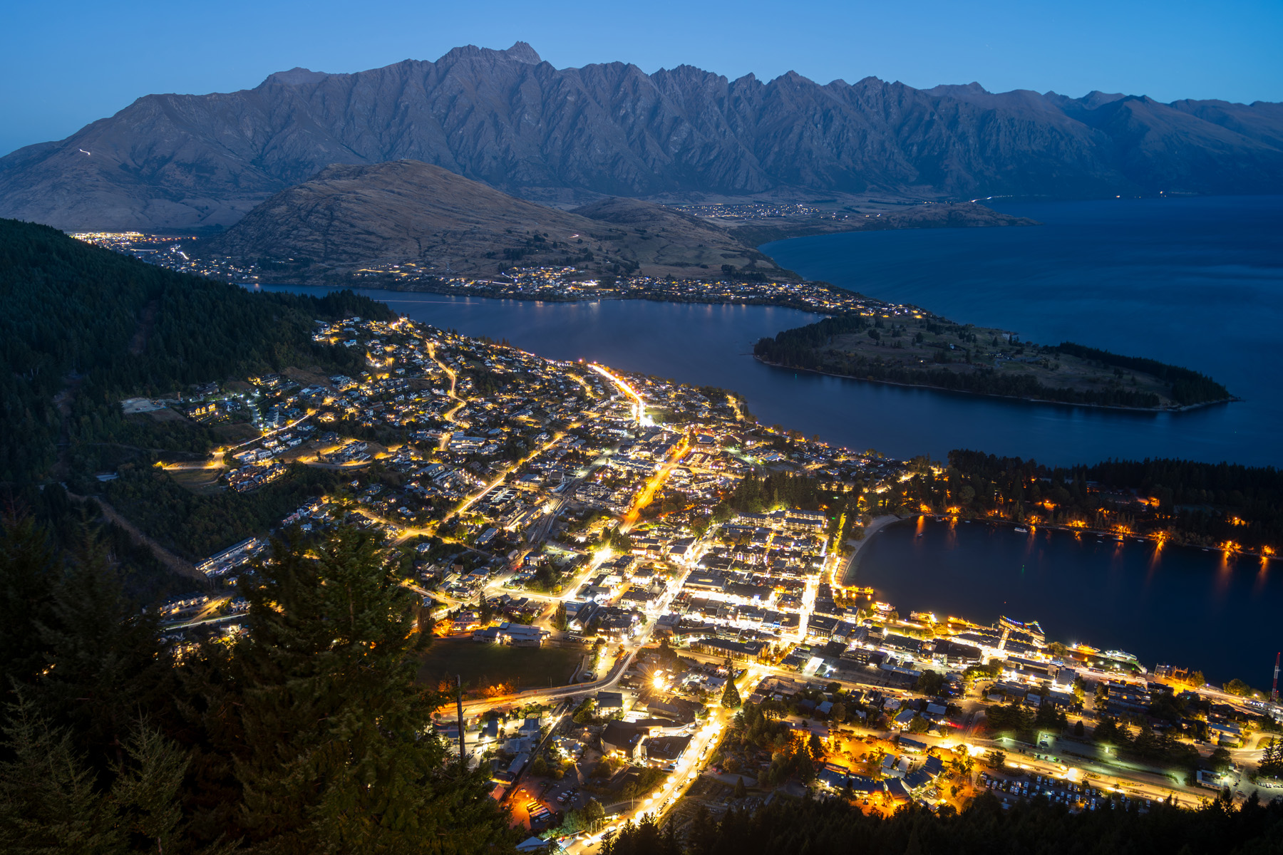 Uma vista noturna de uma cidade aninhada ao lado de um lago sereno e cercada por montanhas.