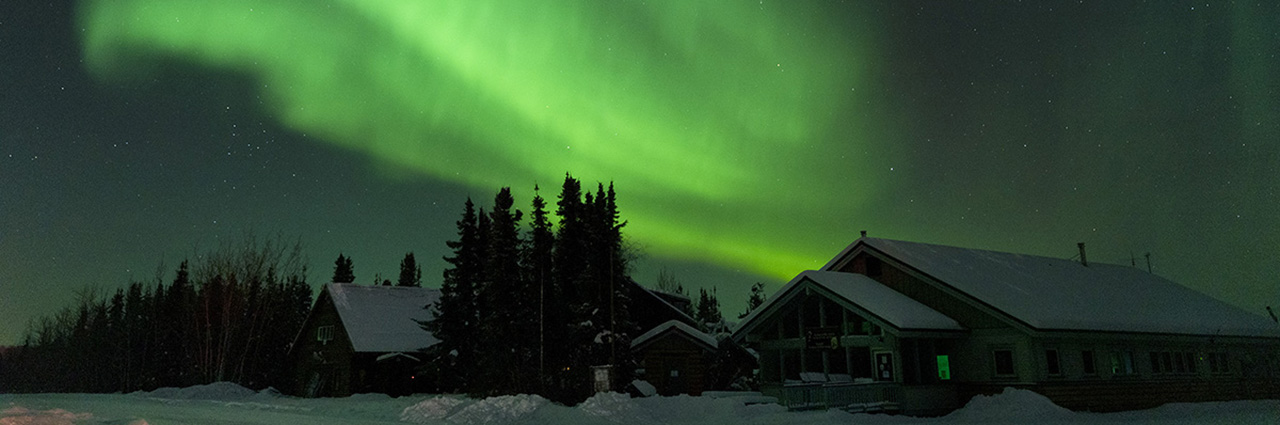 Stunning Northern Lights over snow-covered cabins under a starry night sky.