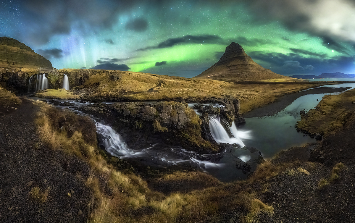 A vivid photograph of the Northern Lights over Kirkjufell mountain in Iceland, showcasing flowing waterfalls and a glowing night sky&mdash;an ideal example for learning how to photograph the northern lights with long exposure techniques and proper lens choice.