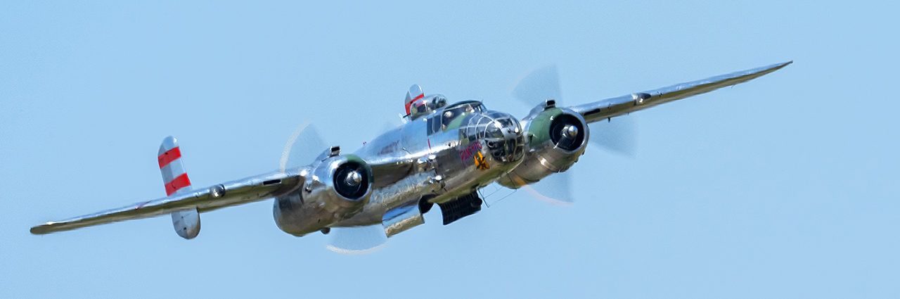 Avión bimotor de época volando sobre un cielo azul despejado.