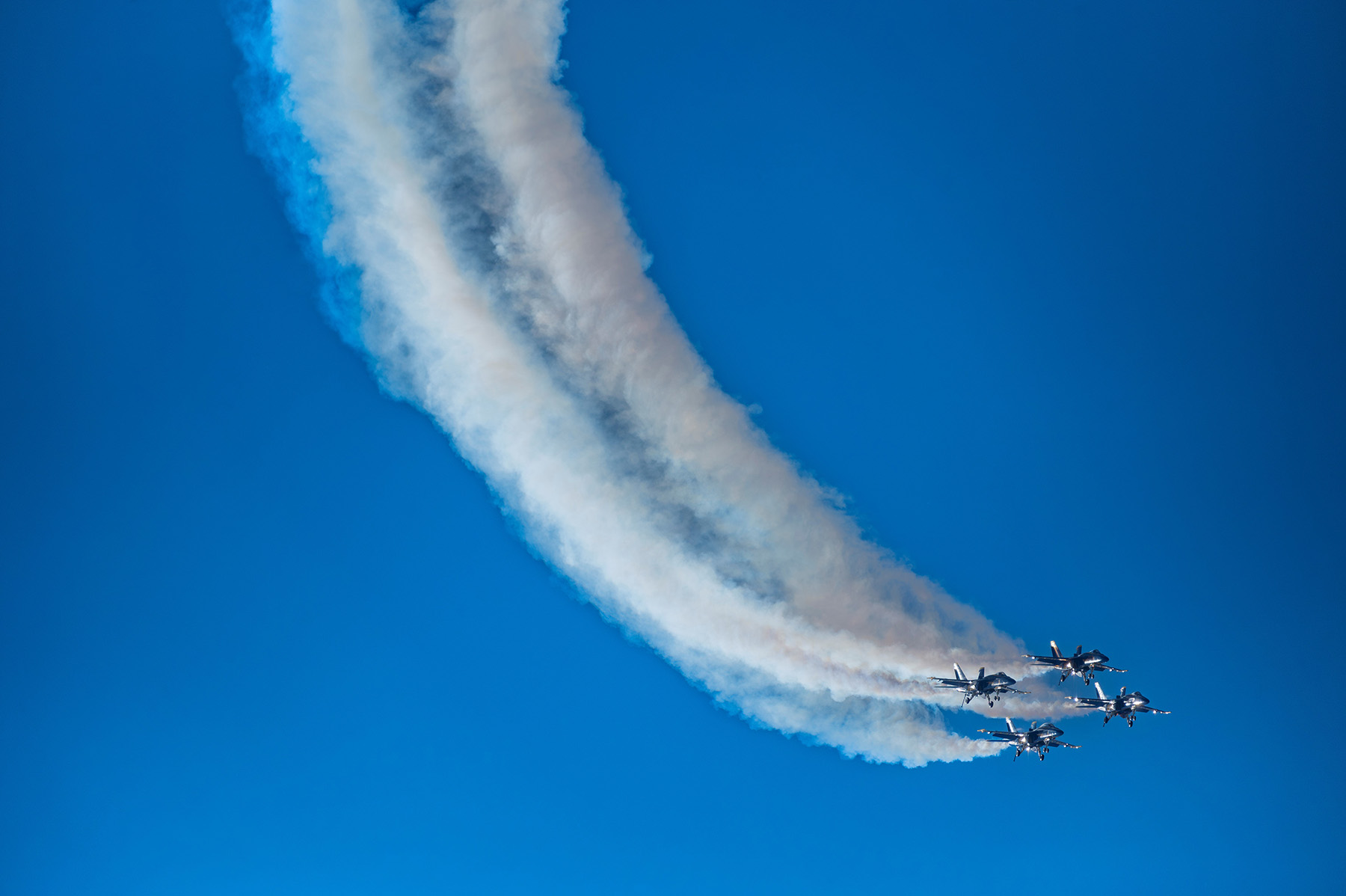 Una formación cerrada de aviones de combate surcando un cielo azul despejado, dejando estelas curvas de vapor: un espectáculo impresionante capturado con técnicas fotográficas expertas en espectáculos aéreos.