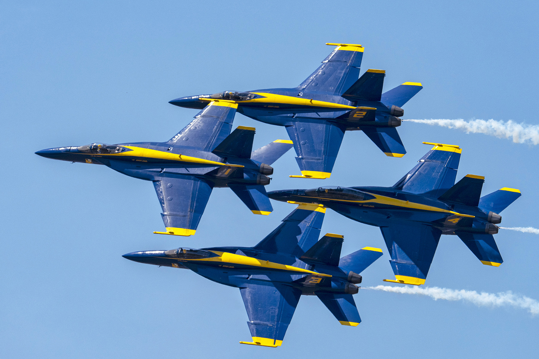 Cuatro aviones de combate Blue Angels vuelan en formación de diamante durante un espectáculo aéreo de precisión, capturado con técnicas fotográficas expertas en espectáculos aéreos.