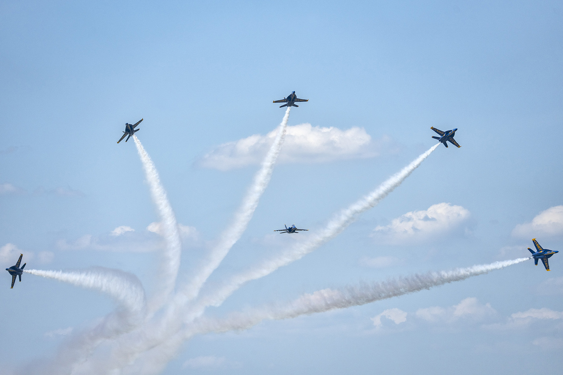 Cinco aviones de combate Blue Angels realizan una maniobra aérea sincronizada, dejando espectaculares estelas de vapor sobre un cielo parcialmente nublado, captadas mediante técnicas avanzadas de fotografía de espectáculos aéreos.